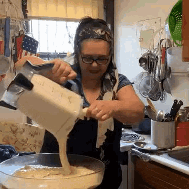 a woman is pouring liquid from a blender into a bowl in a kitchen .
