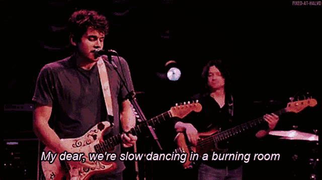 a man singing into a microphone while playing a guitar and another man playing a bass guitar