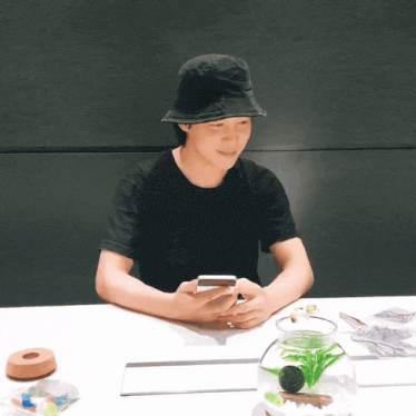 a man in a black hat is sitting at a table looking at his phone