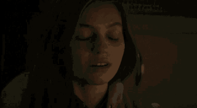 a woman is covering her eyes with her hand while sitting in a dark room .