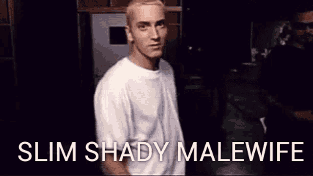 a man in a white shirt is standing in a dark room with the words slim shady malewife written on the screen .