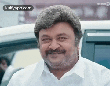a man with a beard and mustache is smiling while standing next to a car .