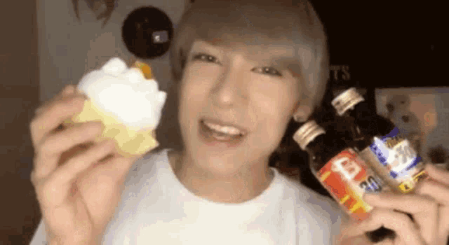 a young man is holding a cupcake and two bottles .