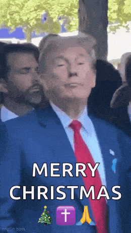 a man in a suit and tie is standing in front of a crowd and saying merry christmas .