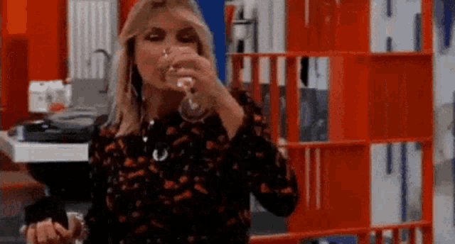a woman is drinking a glass of wine while standing in front of an orange shelf .
