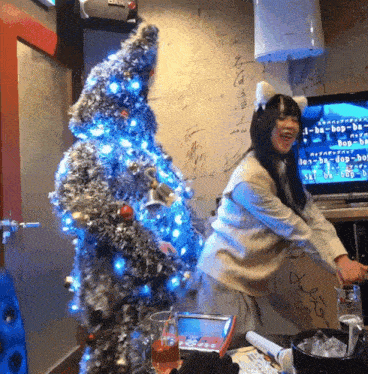 a woman stands in front of a christmas tree and a tv screen that says hop-hop-hop on it