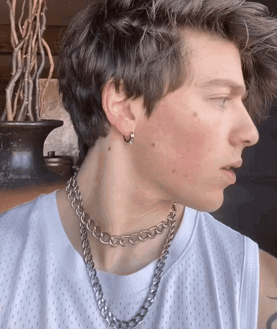 a young man wearing a silver chain around his neck and hoop earrings