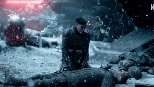 a man in armor is kneeling down next to a man laying on the ground in the snow .