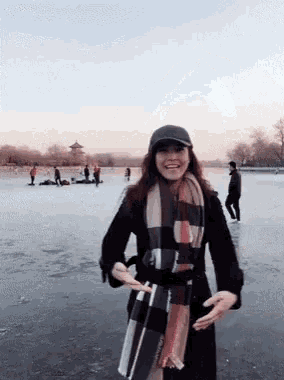 a woman wearing a black hat and a plaid scarf is standing on a frozen lake