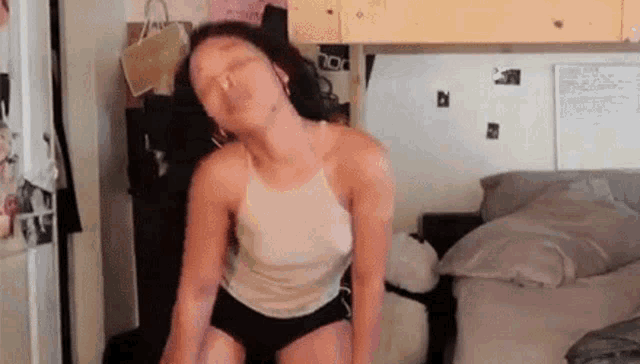 a woman in a white tank top and black shorts is dancing in a bedroom .