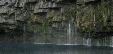 a waterfall is surrounded by rocks and moss and is surrounded by a body of water