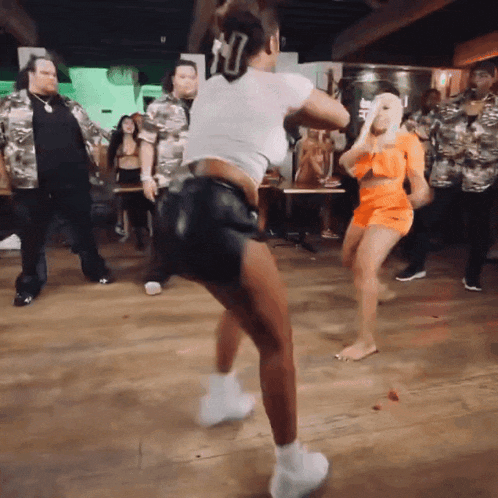 a group of people are dancing in a room and one of them is wearing a white shirt with the letter u on it