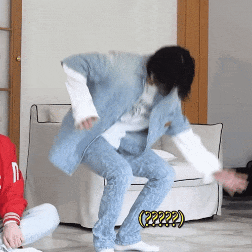 a man in a denim jacket is dancing in front of a white couch with a yellow sign that says ( ?? )