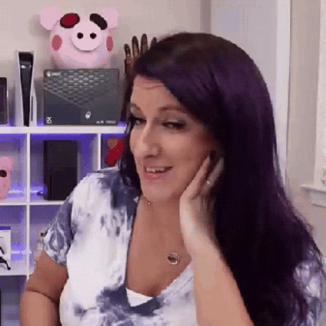 a woman with purple hair is sitting in front of a shelf with an xbox box on it