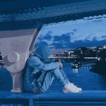 a person in a blue hoodie sits on a bridge overlooking a body of water
