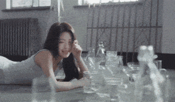 a woman in a white tank top is laying on the floor surrounded by empty glasses and bottles