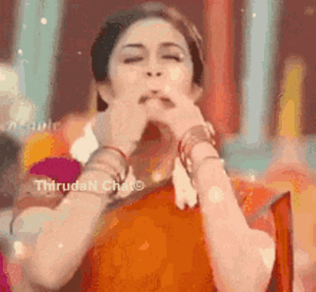 a woman in an orange saree is blowing a kiss with her hand .