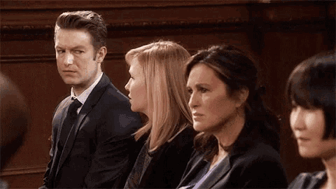 a man in a suit and tie sits next to two women in suits
