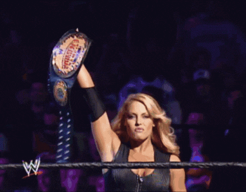 a woman in a wrestling ring is holding up a championship belt