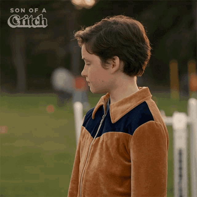 a boy in a brown and blue jacket stands in front of a sign that says son of a griffin