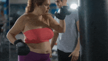a woman wearing boxing gloves stands next to a man in a gym