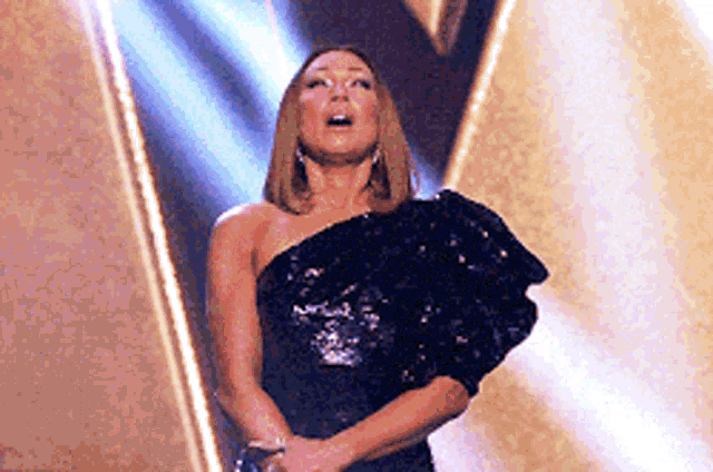 a woman in a black dress is standing on a stage with her eyes closed .
