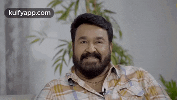a man with a beard and mustache is sitting on a couch and smiling .