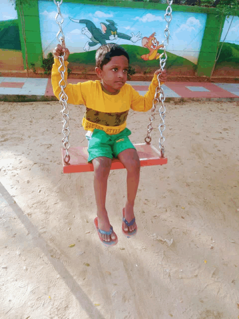 a young boy sits on a swing in front of a wall with tom and jerry painted on it