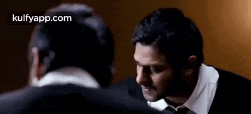 a man in a suit and tie is talking to another man in a room .