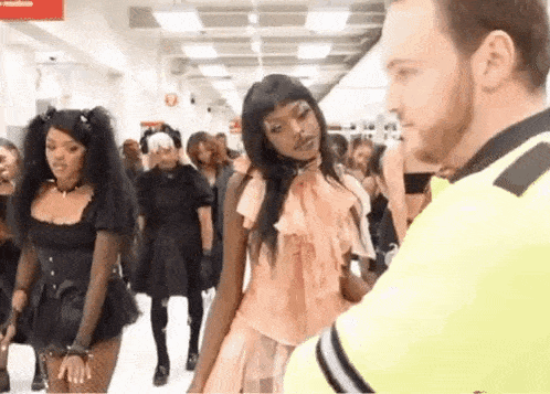 a man in a yellow vest is talking to a woman in a pink dress in a crowded hallway .