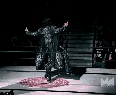 a wrestler is standing in a ring with a el rey logo in the background