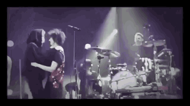 a couple of people are hugging each other on a stage while a band plays behind them .
