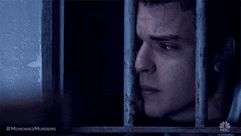 a man is behind bars in a jail cell with his eyes closed and crying .