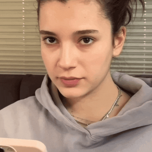 a woman wearing a hoodie and a necklace is looking at her phone