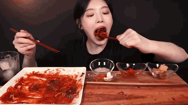 a woman is eating a plate of food with chopsticks and a glass of water