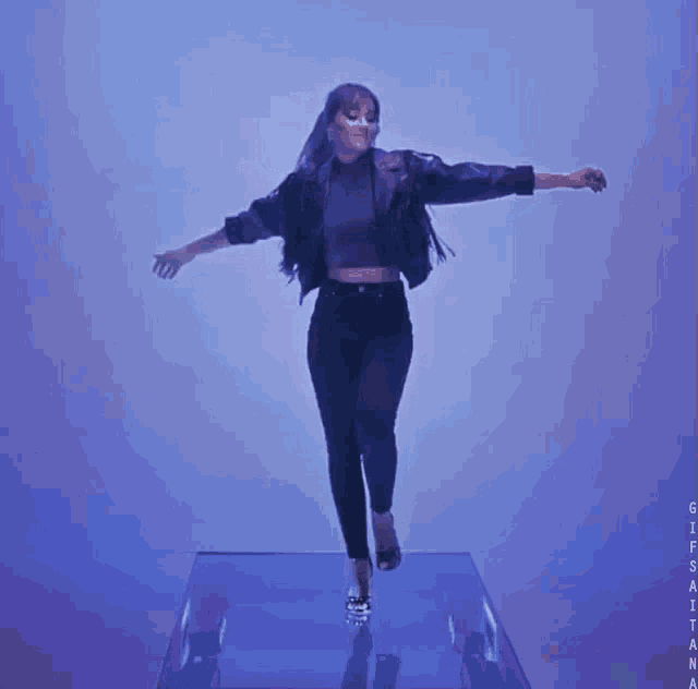 a woman in a purple jacket and black pants is dancing on a glass platform