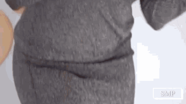 a person wearing a grey sweater and pants is standing in front of a white wall .