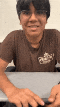 a man wearing a brown shirt that says primitive is sitting at a desk