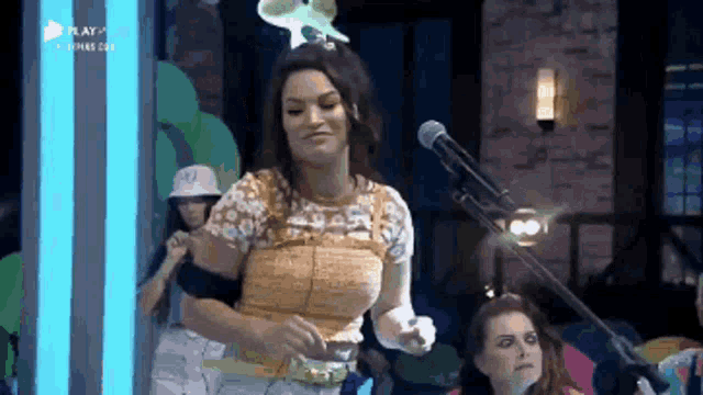 a woman stands in front of a microphone with the word play on the bottom right