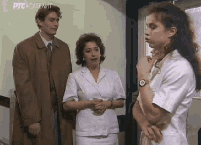 a man and two women are standing next to each other in a room . the woman is wearing a watch .