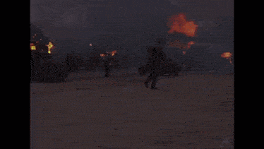 a man is standing in front of a burning house holding a gun