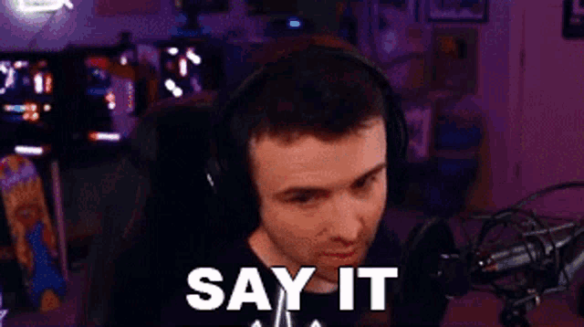a man wearing headphones is sitting in front of a microphone with the words `` say it '' written on the screen .