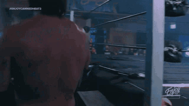 a man in a red shirt is standing in a wrestling ring with the hashtag # enjoycannedheat2 on the bottom