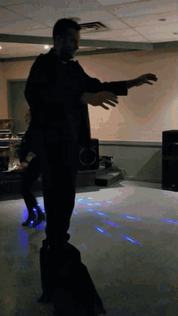 a man in a black suit is dancing in a dark room with blue lights