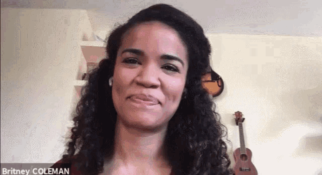 a woman with curly hair is smiling in front of a guitar and a clock on the wall .