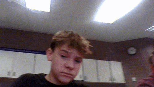 a boy in a kitchen with a clock on the wall above him