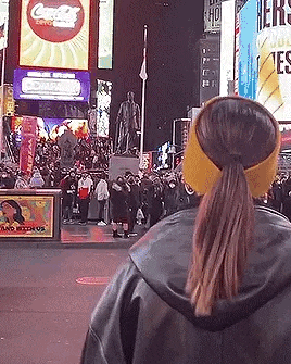 a woman wearing a ponytail and a yellow hat is looking at a crowd of people .