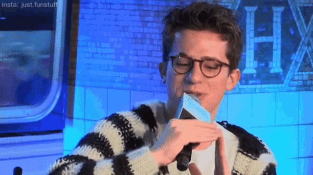 a man wearing glasses and a striped sweater holds a piece of paper in front of a sign that says hx