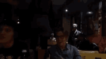 a man wearing a paul frank t-shirt sits at a table in a dark room