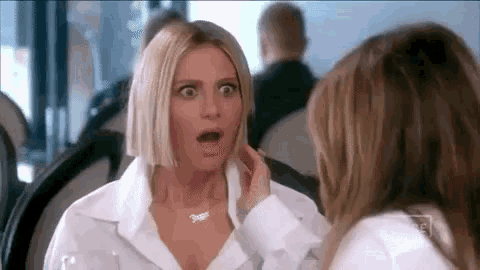 two women are sitting at a table with their mouths open and one of them is touching the other 's face .